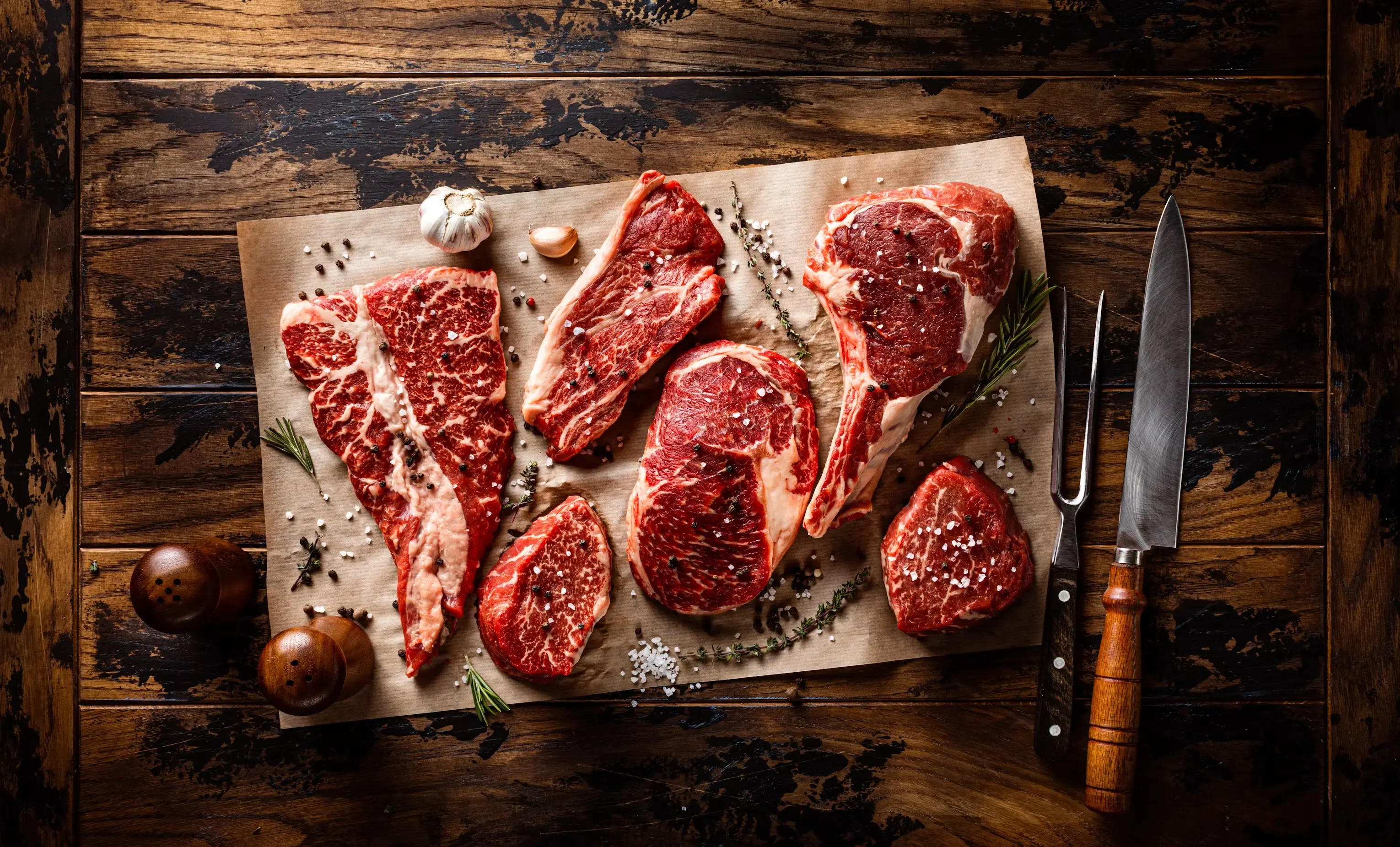 Pieces of raw meat on a wooden cutting board next to a kitchen knife.