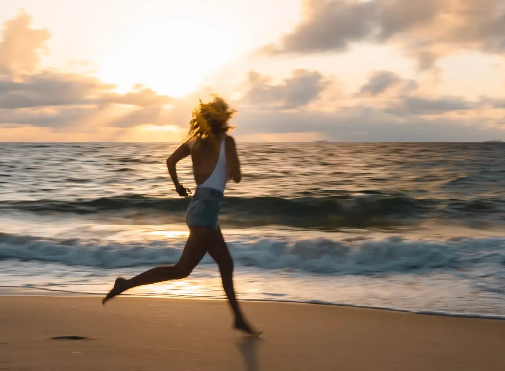 A person running barefoot along the shore at sunrise.