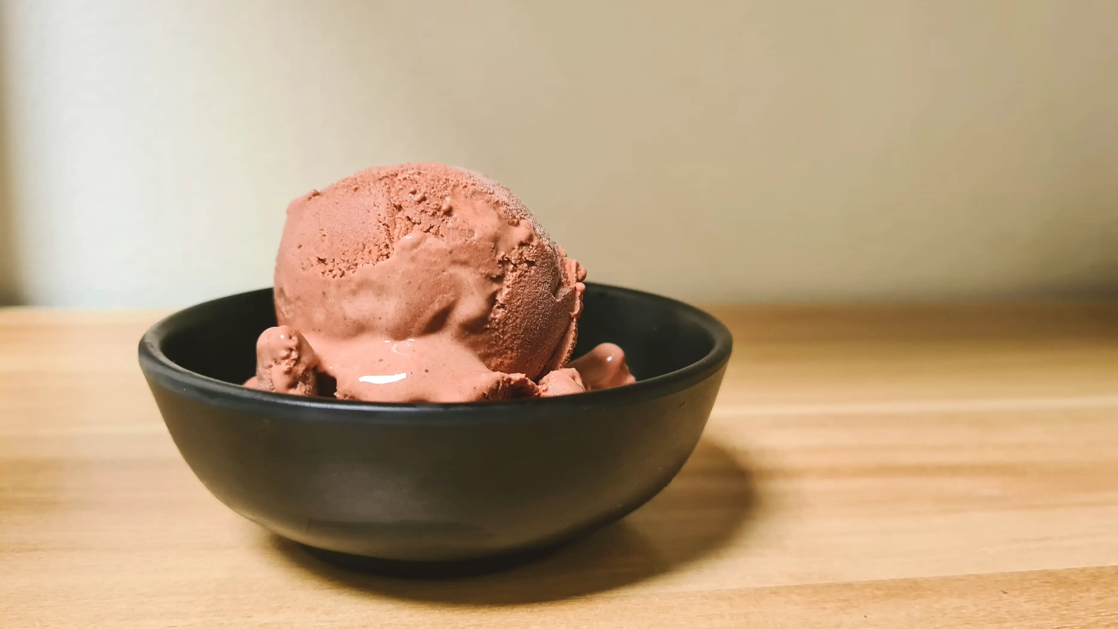 A scoop of chocolate ice cream beginning to melt in a black ceramic bowl.