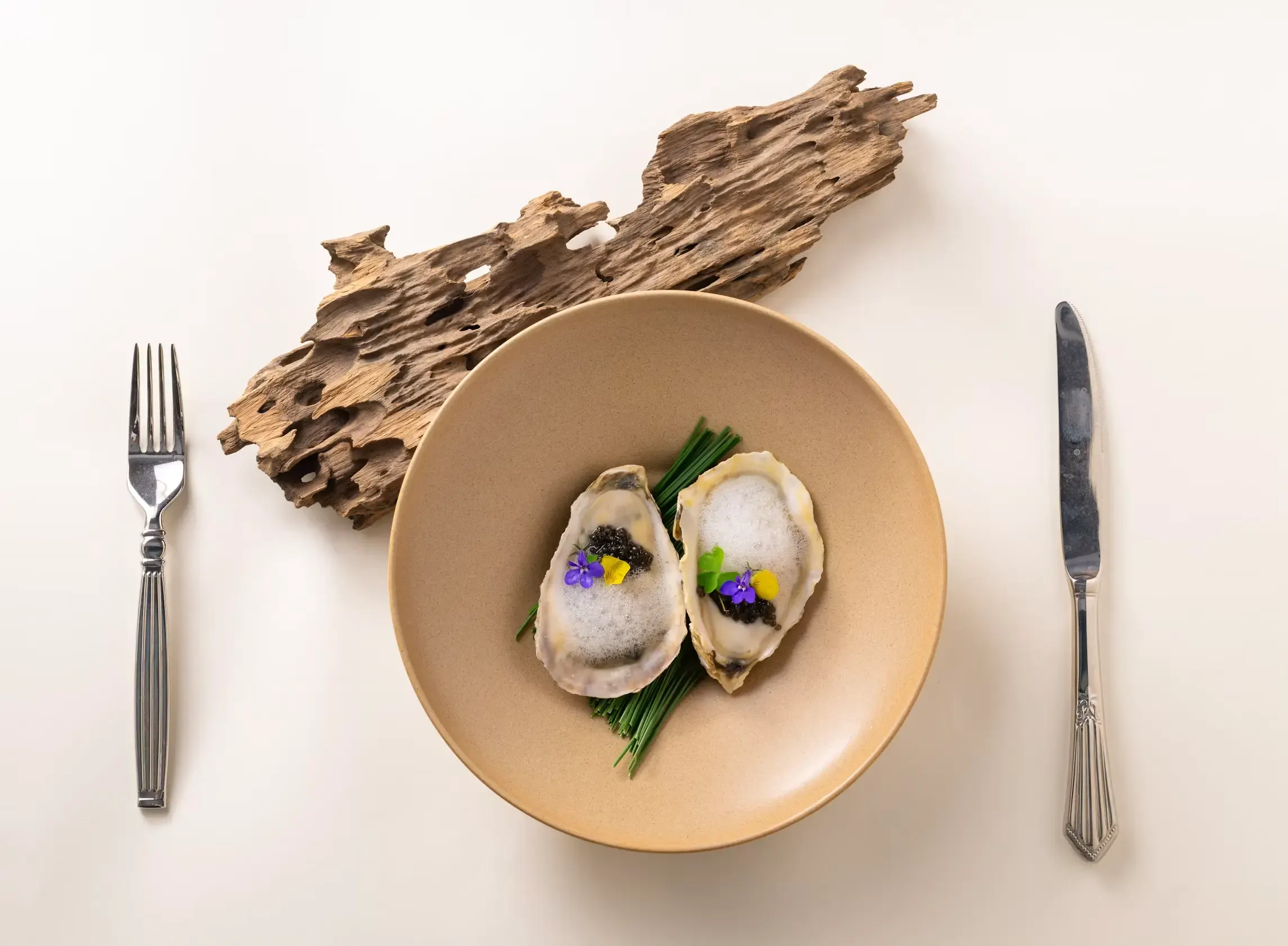 Two opened oysters served on a plate, garnished with green leaves and edible flowers.